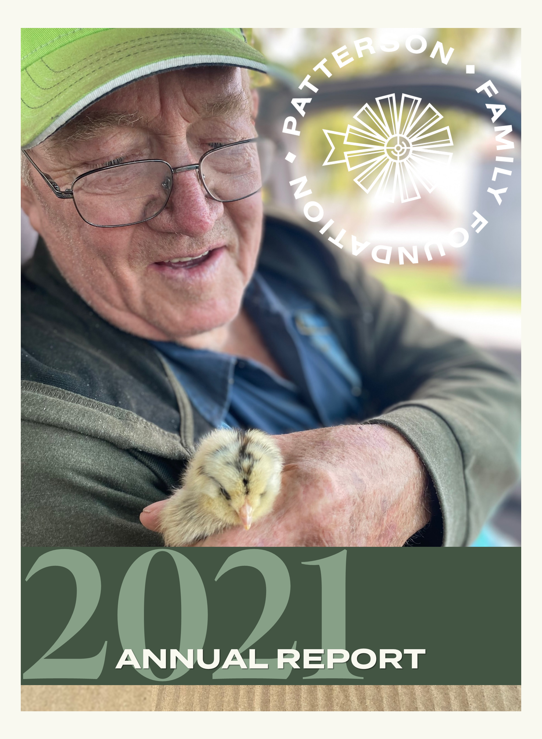 An elderly farmer with glasses, a chambray shirt, and a bright green baseball cap holds a yellow newborn chick.