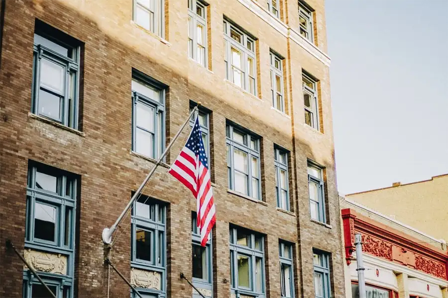 An American flag on a flagpole attached to the side of a small town main street brick building.